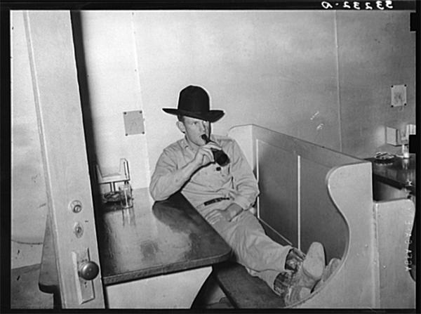 Cowboy drinking a bottle of beer in booth of beer parlor